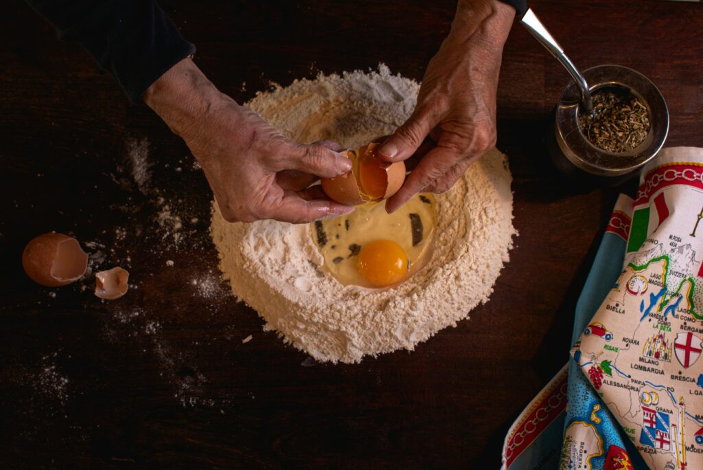 Senior adult cracking egg into flour for pasta. Authentic culinary tradition in cozy kitchen.